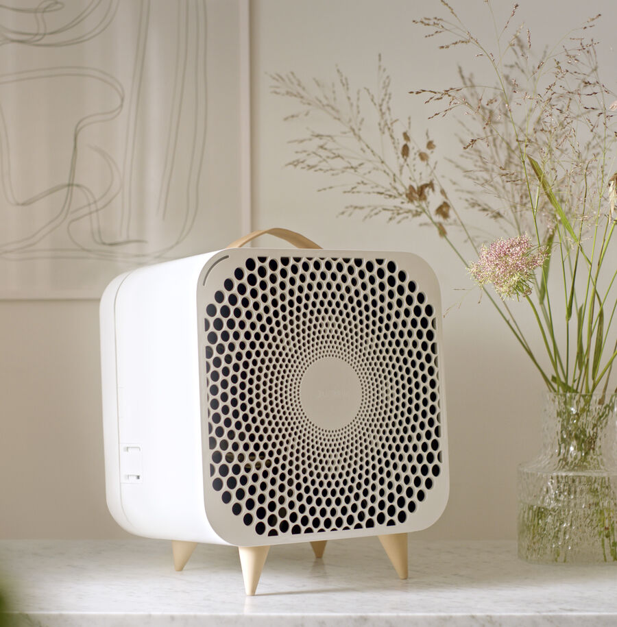 Blueair Pure Fan Auto sitting on tabletop in medium room next to vase of flowers